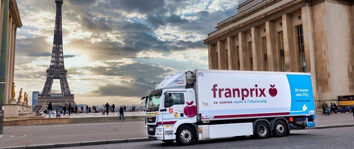 26 tonnes sans CO2 et c’est tant mieux ! Franprix déploie le 1er camion 26 tonnes 100 % électrique en France Camion électrique avec le logo Franprix et en arrière plan la Tour Eiffel