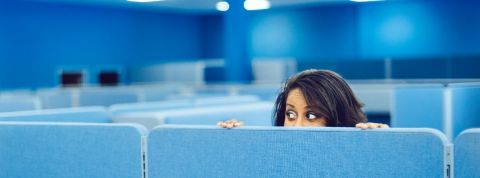 Six applications qui fliquent les salariés Une femme se cache derrière une paroi dans un grand open-space