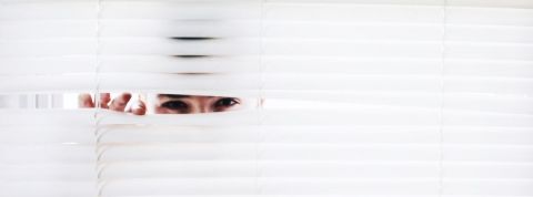 Comment éviter d'être surveillé par son boss en télétravail ? Une personne qui regarde derrière un rideau