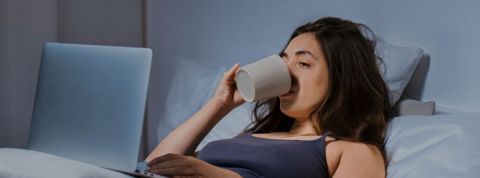 Le pyjama n'est pas l'ennemi du télétravail Une femme en pyjama dans son lit devant son ordinateur portable en train de boire une tasse de café