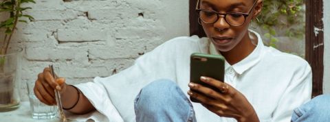 Comment Clubhouse crée-t-il une nouvelle culture orale ? Une jeune femme noire en train de regarder son téléphone alors qu'elle mange