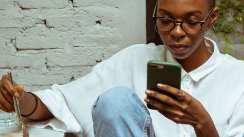 Comment Clubhouse crée-t-il une nouvelle culture orale ? Une jeune femme noire en train de regarder son téléphone alors qu'elle mange