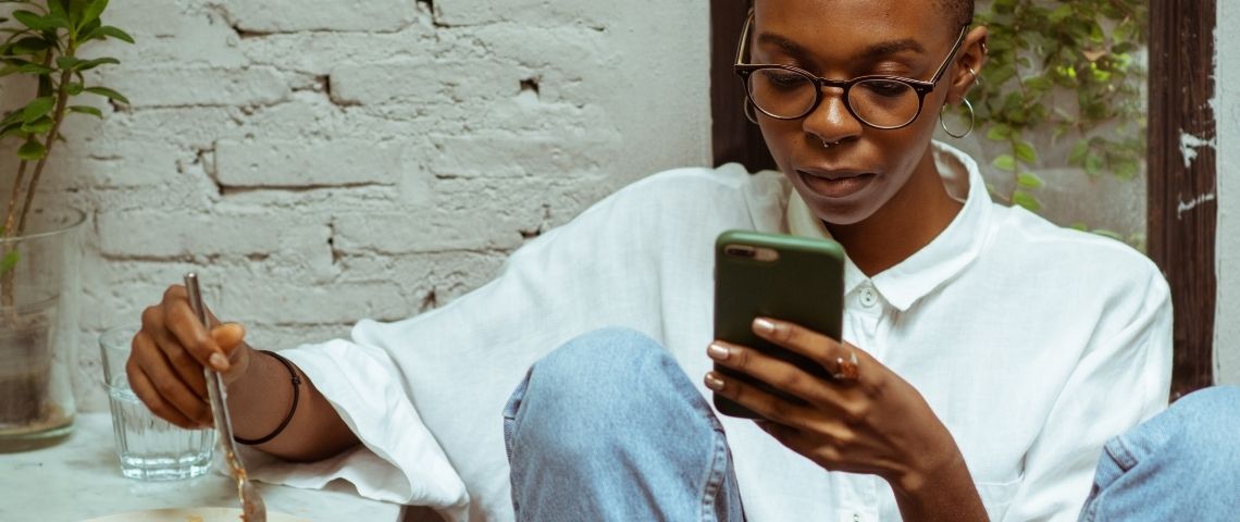 Comment Clubhouse crée-t-il une nouvelle culture orale ? Une jeune femme noire en train de regarder son téléphone alors qu'elle mange