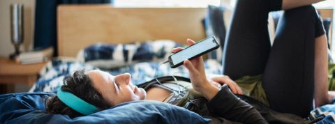 Ils passent des heures sur Clubhouse... Pourquoi ce réseau rend déjà accro ? Une femme sur son lit parle dans le micro de son smartphone et porte un casque