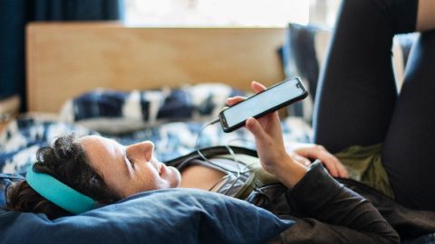 Une femme sur son lit parle dans le micro de son smartphone et porte un casque