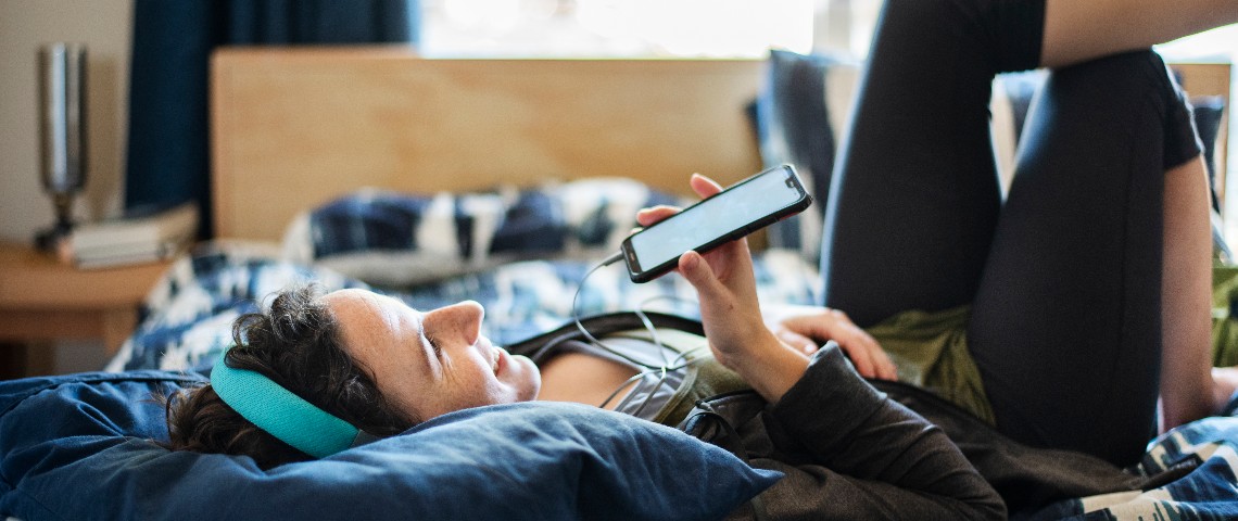 Ils passent des heures sur Clubhouse... Pourquoi ce réseau rend déjà accro ? Une femme sur son lit parle dans le micro de son smartphone et porte un casque