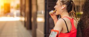 Une femme en train de déguster une barre de céréales en pleine séance de sport, les écouteurs dans les oreilles.