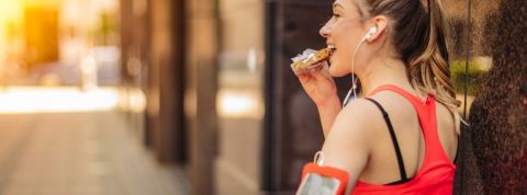 Comment Feed cartonne sur Clubhouse ? Une femme en train de déguster une barre de céréales en pleine séance de sport, les écouteurs dans les oreilles.