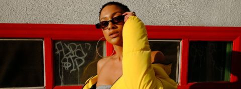 Comment l'appli Depop repère les tendances avant tout le monde Une femme pose avec des lunettes rectangulaire et une grosse doudoune jaune