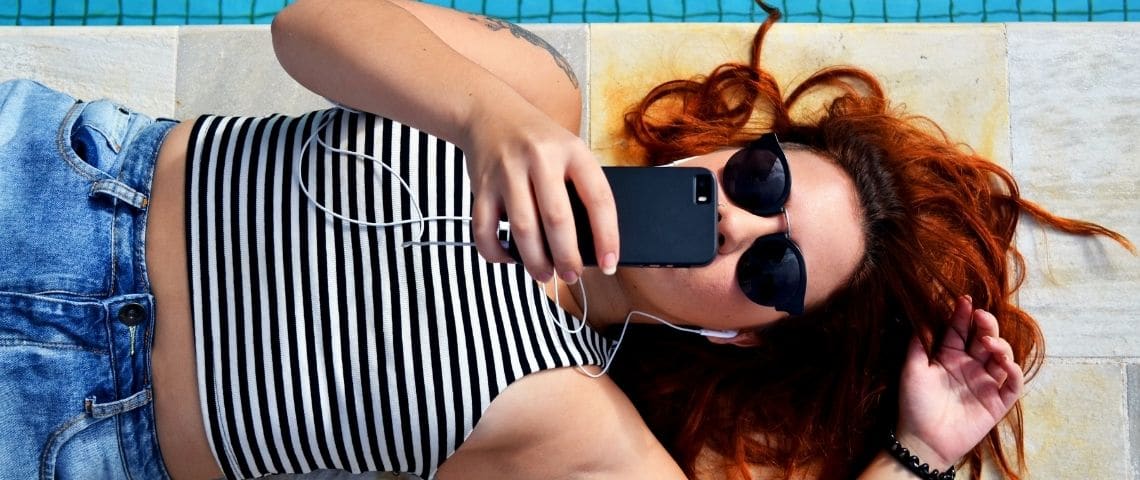 Moka Jeune femme allongée au bord d'une piscine, elle regarde son téléphone
