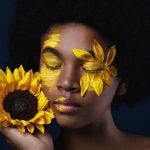 Une femme noire avec un tournesol et des pétales sur le visage