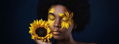 Comment la cosmétique sauvage s'invite en tête des tendances beauté ? Une femme noire avec un tournesol et des pétales sur le visage