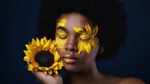 Une femme noire avec un tournesol et des pétales sur le visage