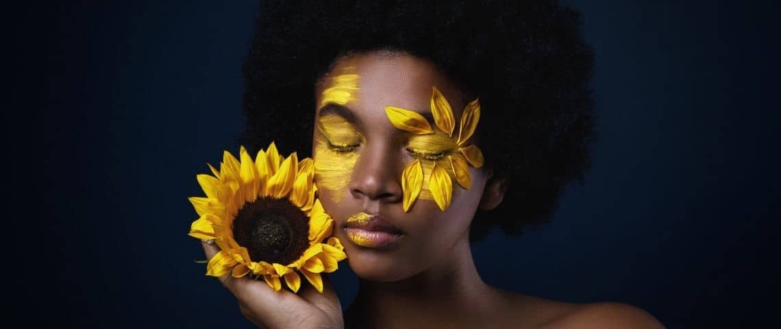 Comment la cosmétique sauvage s'invite en tête des tendances beauté ? Une femme noire avec un tournesol et des pétales sur le visage