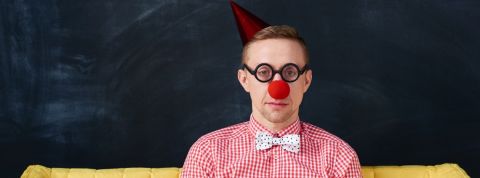 Les entreprises arrêtent d'essayer d'être drôles pour le premier avril (enfin pas tout le monde) Un homme déguisé en clown à l'air triste sur un canapé jaune