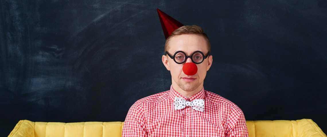 Les entreprises arrêtent d'essayer d'être drôles pour le premier avril (enfin pas tout le monde) Un homme déguisé en clown à l'air triste sur un canapé jaune