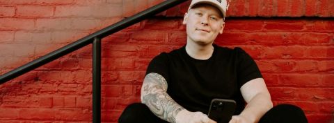 Une appli pour créer des NFT en quelques minutes Un homme habillé en noir et tatoué sourit avec son smartphone