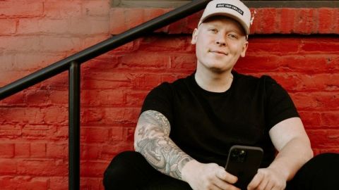 Un homme habillé en noir et tatoué sourit avec son smartphone