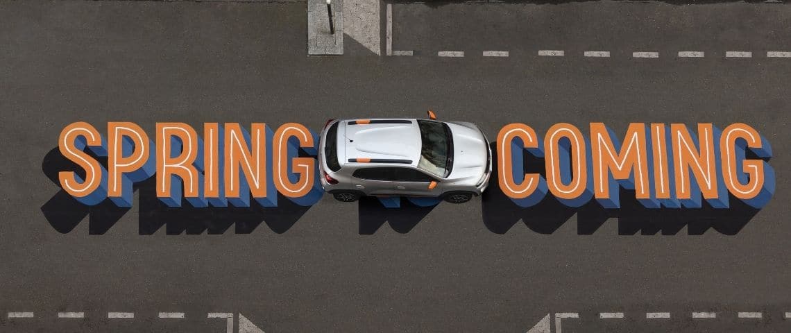 Dacia célèbre le printemps dans la rue et clame haut et fort l’arrivée de Spring, la révolution électrique pour tous. Voiture Dacia prise en hauteur avec le message - Spring is coming - inscrit sur la route en orange et bleu