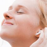 Jeune femme, les yeux fermés, sourir aux lèvres, la main sur son oreille dotée d'un écouteur