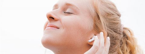 Jackson-Simmer Jeune femme, les yeux fermés, sourir aux lèvres, la main sur son oreille dotée d'un écouteur