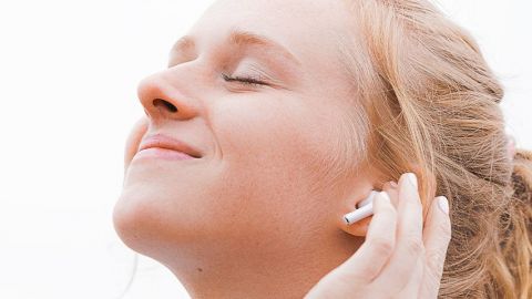 Jeune femme, les yeux fermés, sourir aux lèvres, la main sur son oreille dotée d'un écouteur