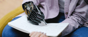 Homme avec une main bionique écrit sur un carnet au stylo