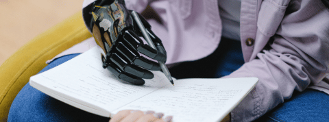 Robotic Hand Writing Homme avec une main bionique écrit sur un carnet au stylo