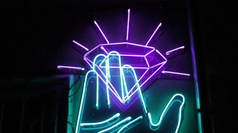 Une main bleue en néon tient un diamant violet aussi en néon