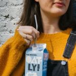 Une femme en salopette buvant une brique d'Oatly à la paille