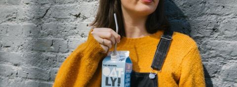 Pourquoi Oatly cartonne autant ? Une femme en salopette buvant une brique d'Oatly à la paille