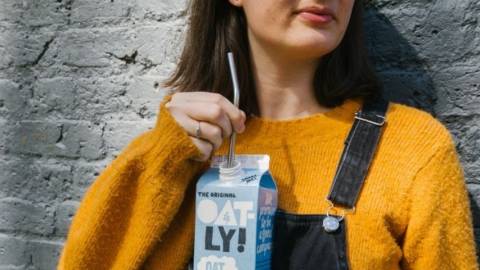 Une femme en salopette buvant une brique d'Oatly à la paille