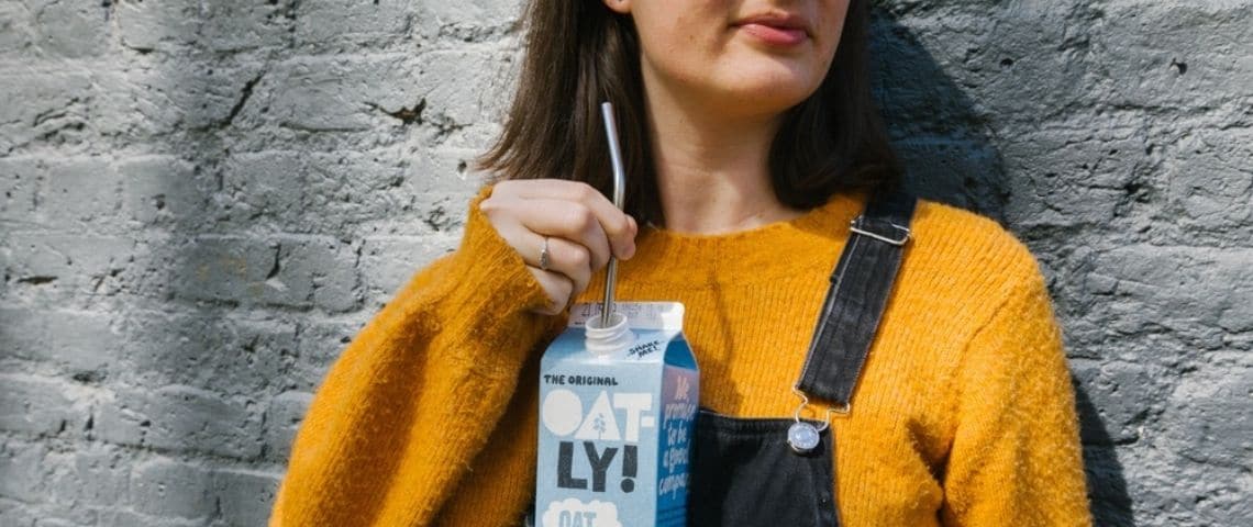 Pourquoi Oatly cartonne autant ? Une femme en salopette buvant une brique d'Oatly à la paille