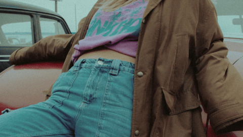 Une fille en jean appuyée contre une voiture rouge