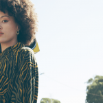 Une jeune femme en chemise est debout dans une rue vide avec un ghetto blaster sur l'épaule