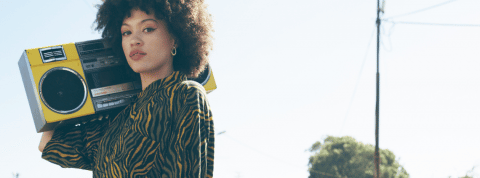 Une jeune femme en chemise est debout dans une rue vide avec un ghetto blaster sur l'épaule