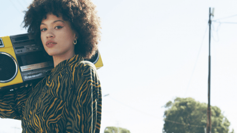 Une jeune femme en chemise est debout dans une rue vide avec un ghetto blaster sur l'épaule