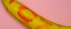 Une banane recouverte de traces de rouge à lèvre sur fond rose