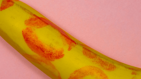 Une banane recouverte de traces de rouge à lèvre sur fond rose