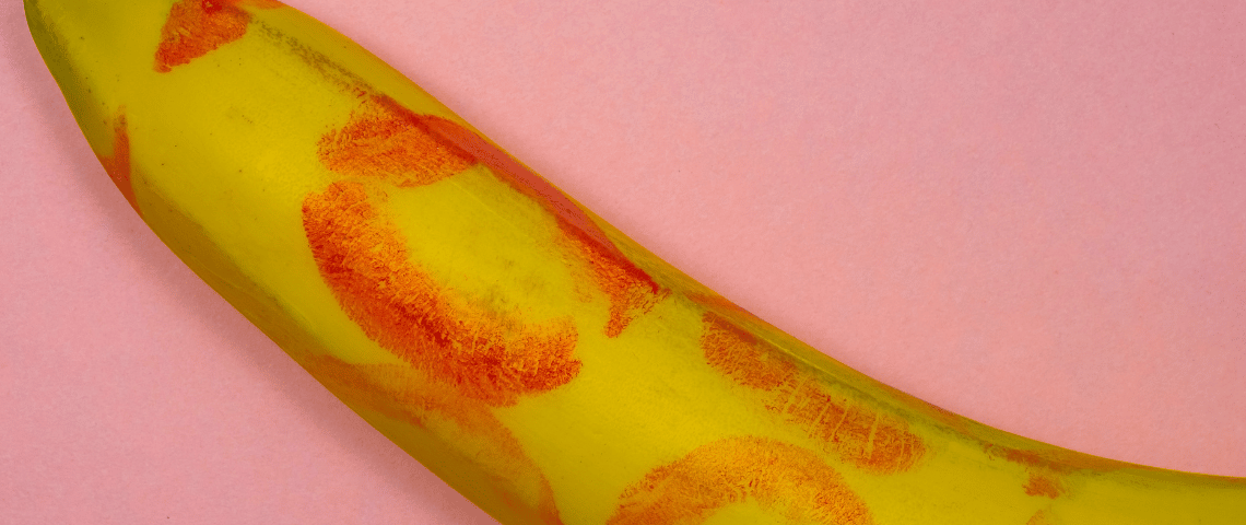 Post-vaccin, l'été sera chaud. Une banane recouverte de traces de rouge à lèvre sur fond rose