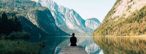 personne assise sur le ponton d'un lac entouré de montagnes