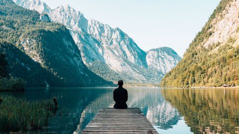 personne assise sur le ponton d'un lac entouré de montagnes
