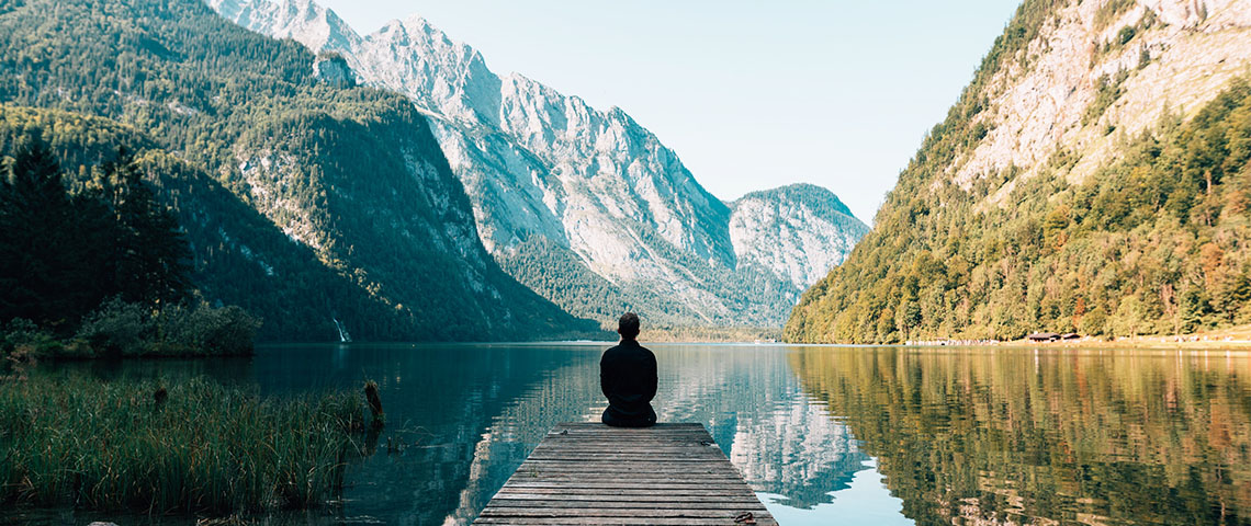 personne assise sur le ponton d'un lac entouré de montagnes