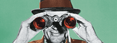 Un homme en costume tient devant son visage des jumelles