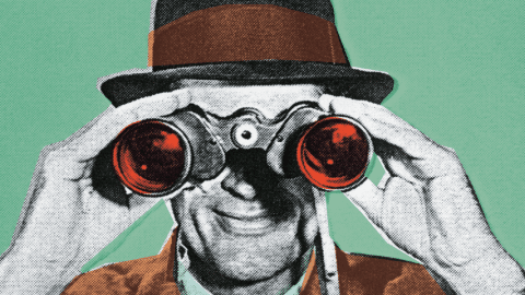 Un homme en costume tient devant son visage des jumelles