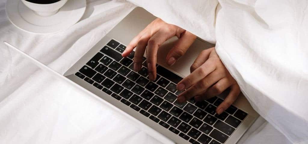 Pourquoi les gens ne v eulent pas retourner au bureau ? Une personne sous la couette en train d'écrire sur un clavier d'ordinateur