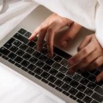 Une personne sous la couette en train d'écrire sur un clavier d'ordinateur