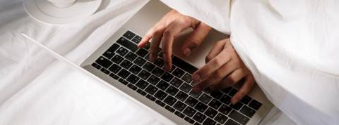 Pourquoi les gens ne v eulent pas retourner au bureau ? Une personne sous la couette en train d'écrire sur un clavier d'ordinateur