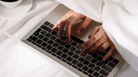 Une personne sous la couette en train d'écrire sur un clavier d'ordinateur