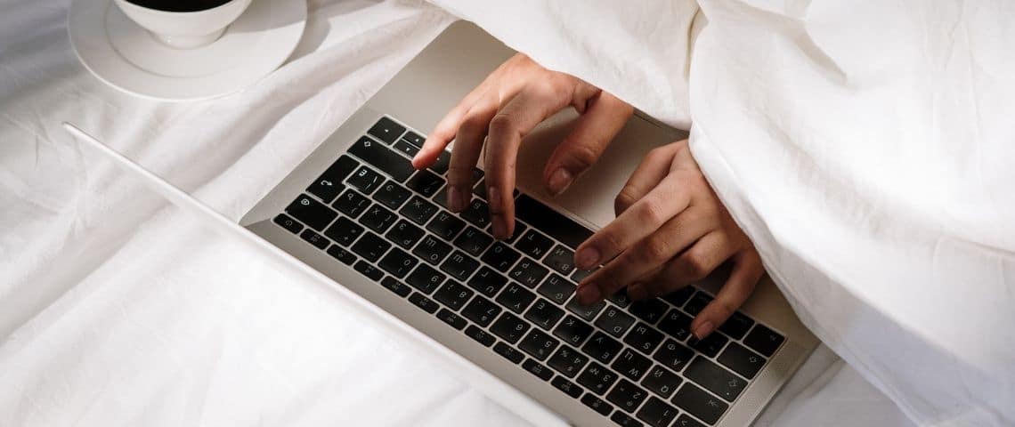 Pourquoi les gens ne v eulent pas retourner au bureau ? Une personne sous la couette en train d'écrire sur un clavier d'ordinateur
